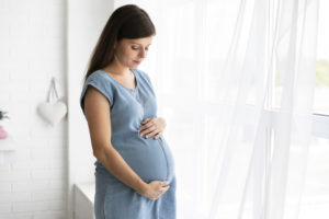 אישה מחזיקה את הבטן שלה עם 2 הידיים שלה בזמן ההריון